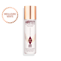 Une brume fixatrice ouverte dans un flacon transparent à côté de son bouchon doré.